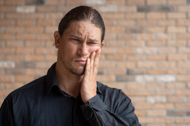 man holding his cheek in pain wondering How Does Tooth Decay Develop